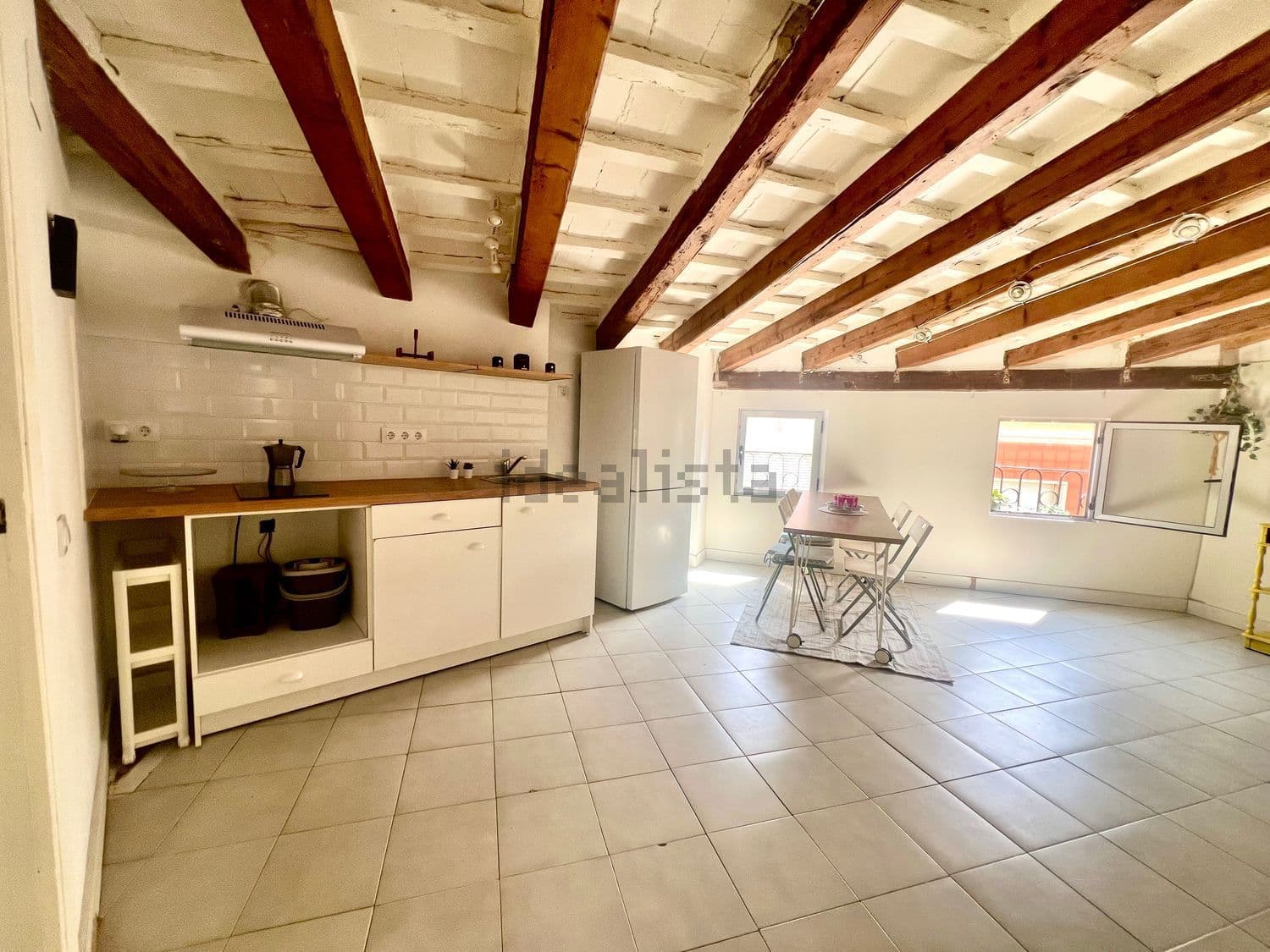 Cocina abierta bajo vigas de madera vistas, con la mesa de comedor junto a la ventana
