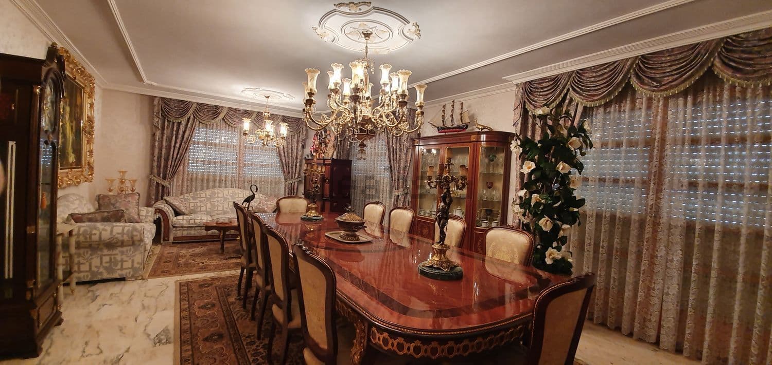 Comedor con mesa larga de madera, lámpara de araña y cortinas