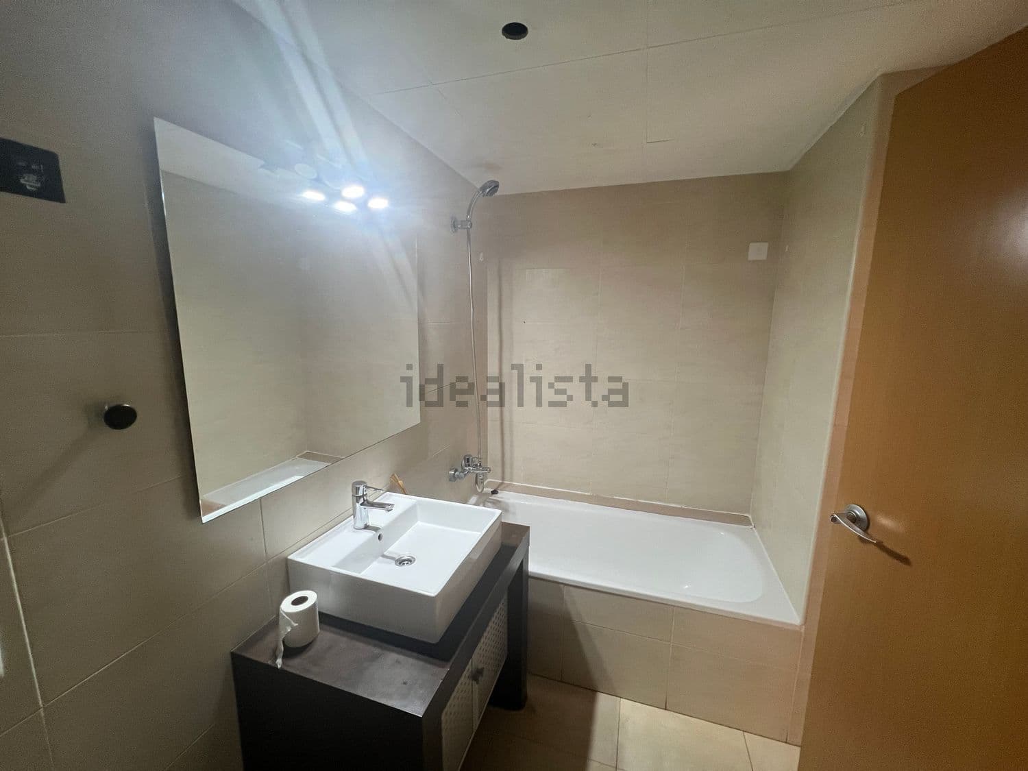 Baño con lavabo sobre mueble oscuro y bañera