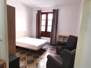 Zona de dormitorio con cama y butacas junto al balcón