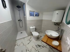 Baño con ducha, lavabo sobre encimera de madera y termo