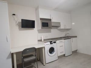 Cocina con lavadora, microondas y televisor junto a un escritorio