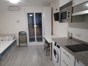 Cocina con placa y lavadora frente a la cama