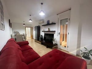 Salón con sofá rojo, mueble de televisión y salida al balcón