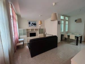 Salón con sofá negro, mueble de televisión y comedor