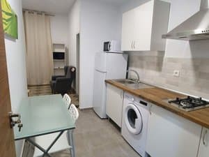 Cocina con placa, lavadora, frigorífico y mesa de cristal