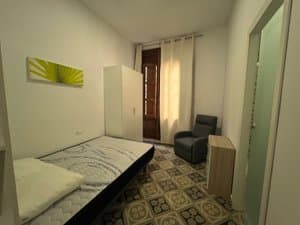 Zona de dormitorio con cama, butaca y balcón