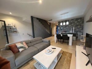 Salón con sofá gris, mesa baja y comedor al fondo