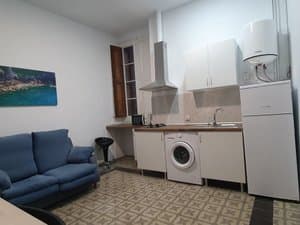 Estudio con sofá azul y cocina con lavadora
