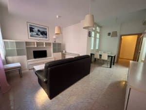 Salón con sofá negro, mueble de televisión y comedor