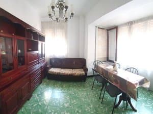 Salón comedor con vitrina, sofá y mesa junto a los ventanales