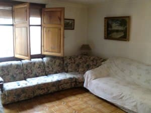 Salón con sofá rinconera y ventanas con porticones de madera