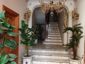 Vestíbulo con escalera de mármol, plantas y lámpara de araña