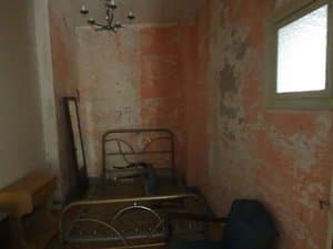 Dormitorio con cama de hierro y paredes a reformar