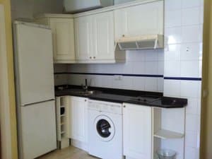 Cocina con muebles blancos, lavadora y frigorífico