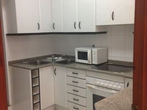 Cocina con muebles blancos, horno y microondas